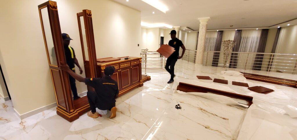 Three AA+ Movers professionals in uniform providing Relocation Handyman Services while reassembling a glass cabinet after a move