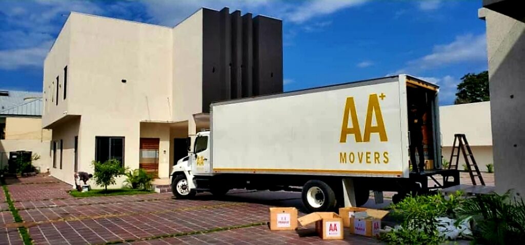 AA+ Movers' 24-foot box truck with tail lift parked outside a home in a gated community in the Airport Residential Area during a house relocation