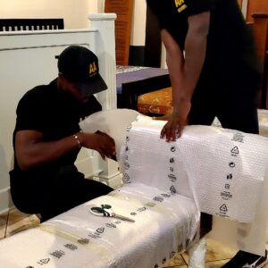 "Premier moving services in Ghana by AA+ Movers, featuring uniformed movers carefully wrapping a piece of furniture with protective materials before transit from Cantonments, Accra."