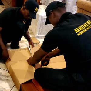 "Premier moving services in Ghana by AA+ Movers, featuring movers carefully removing cardboard packaging from furniture after an office move in Ridge, Accra."